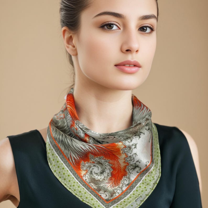 May include: A square silk scarf with a swirling orange and gray design. The scarf has a green and white dotted border. The scarf is around the neck.