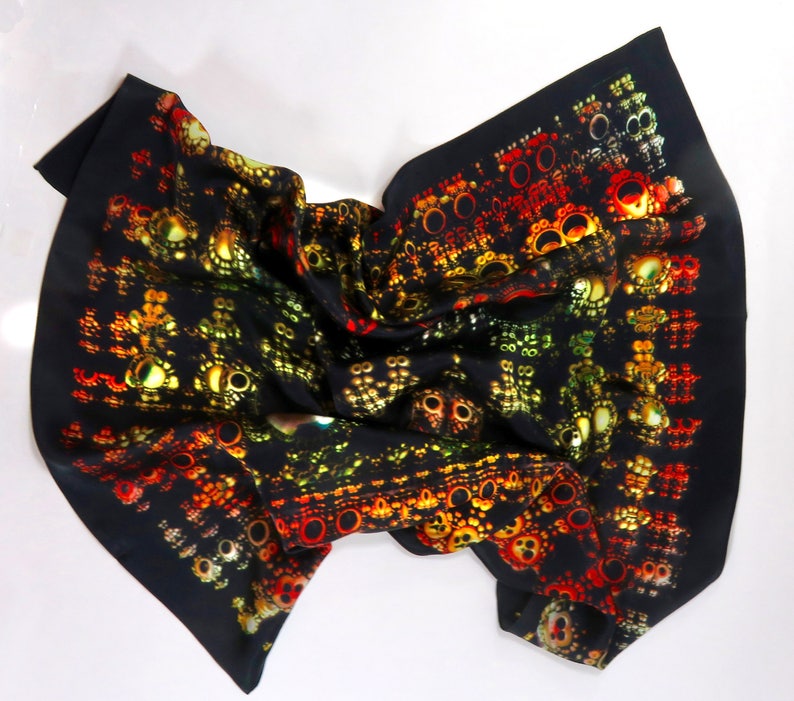 Op de afbeelding: Een zwarte zijden sjaal met een herhalend patroon van kleurrijke, abstracte vormen in rood, geel en groen. De sjaal is gevouwen en gedrapeerd, wat het ingewikkelde ontwerp benadrukt. Modeaccessoire.