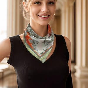 May include: A square silk scarf with a detailed pattern in shades of gray, orange, and green. The scarf is worn around the neck over a black sleeveless top. The background features a blurred architectural setting.