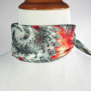 May include: A silk scarf with a unique pattern of gray, red, and white feather-like designs. The scarf is wrapped around a mannequin's neck, showcasing its vibrant colors and intricate details. The scarf's design is eye-catching and adds a touch of elegance.