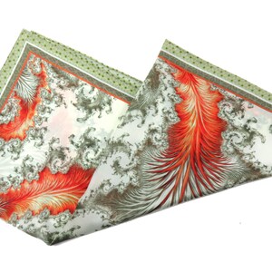 May include: A folded pocket square with a white background. The pocket square features a detailed design with red, gray, and white patterns. The edges are bordered with a green dotted pattern.