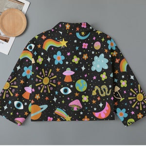 May include: Black jacket with a colorful space-themed pattern. The design includes rainbows, stars, planets, UFOs, mushrooms, and flowers. The jacket has long sleeves and a collar.