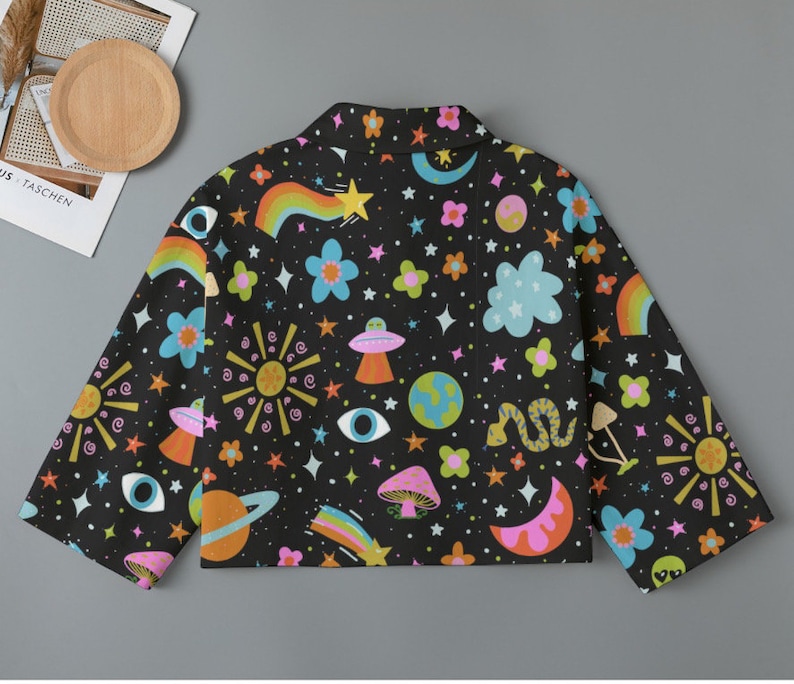 May include: Black jacket with a colorful space-themed pattern. The design includes rainbows, stars, planets, UFOs, mushrooms, and flowers. The jacket has long sleeves and a collar.