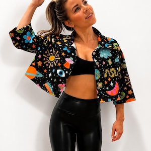 May include: Black button-up shirt with a colorful space-themed pattern featuring planets, stars, and UFOs. The shirt has a white collar and cuffs. The model is wearing black leggings and a black sports bra.