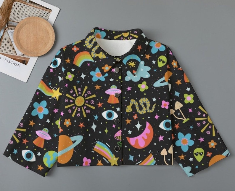 May include: Black button-up jacket with a colorful, whimsical print. The design features planets, rainbows, stars, flowers, UFOs, and other celestial and psychedelic elements. The jacket has a classic collar and long sleeves.