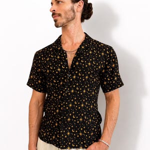 May include: A short-sleeved button-down shirt in black featuring a repeating pattern of yellow stars, crescent moons, and small dots. The shirt has a notched collar, a front button placket, and a straight hemline, crafted from a lightweight fabric.