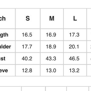 May include: A white chart with black text detailing garment measurements in inches. The chart includes sizes S, M, L, and XL, with measurements for length, shoulder, bust, and sleeve.