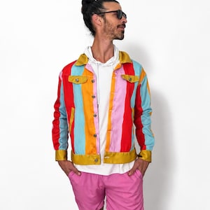May include: A multi-colored striped jacket featuring vertical bands of red, light blue, pink, and orange, with a mustard yellow collar, cuffs, and hem. The jacket has a button-front closure, two chest pockets with flaps, and long sleeves.