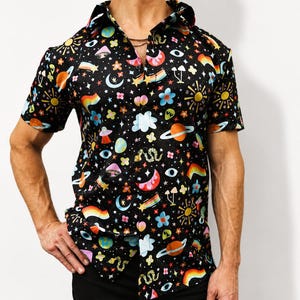 May include: A short-sleeved button-down shirt in black featuring a colorful, repeating pattern of planets, suns, moons, rainbows, mushrooms, flowers, clouds, snakes, and eyes. The shirt has a classic collar and a front button closure.