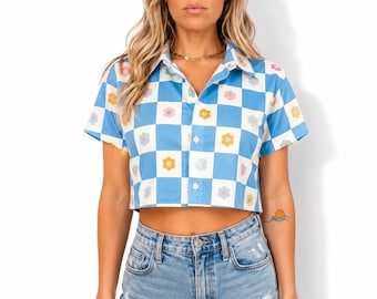 May include: A short-sleeve button-down crop top featuring a blue and white checkerboard pattern with small, colorful flower icons centered in each square, paired with light-wash denim shorts that have a distressed, frayed hemline detail.