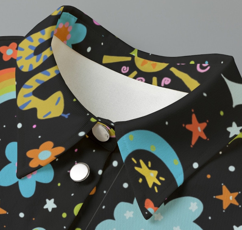 May include: Close-up of a black shirt collar with a whimsical pattern. The design features a yellow snake, rainbows, flowers, stars, and clouds in various colors. The shirt has two silver buttons.
