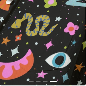 May include: Black fabric with a colorful, whimsical pattern. The design includes a yellow snake with blue markings, pink flowers, stars, and an eye. The fabric has a pocket.