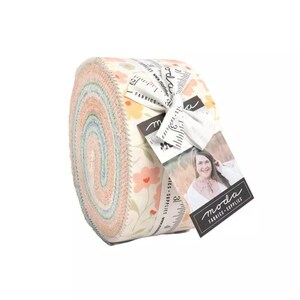 May include: Rolled fabric bundle with a floral design in pastel shades. The fabric is tied with a white ribbon and a tag with the "moda FABRICS - SUPPLIES" logo. The fabric roll is a mix of peach, blue, and cream colours.