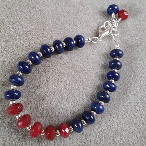 May include: A blue and red beaded bracelet with a silver clasp. The bracelet is made with round beads and has a two-tone color scheme.