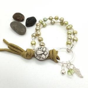 May include: A green and silver beaded bracelet with a suede tassel and a charm with a heart and wings design. The bracelet also has a silver ring with a heart, a green stone, and a silver wing charm.