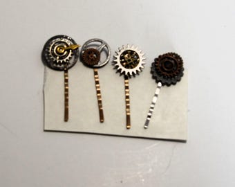 Può includere: Quattro forcine per capelli decorate con ingranaggi e componenti di orologeria. La prima forcina presenta un ingranaggio argentato con una lancetta dorata. La seconda ha un piccolo ingranaggio color bronzo in un anello argentato. La terza è un ingranaggio argentato e la quarta è un ingranaggio scuro.