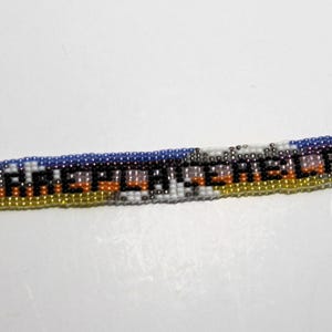 May include: A multi-colored beaded bracelet with a silver clasp and a chain. The beads spell out the word "remarkable" in black.