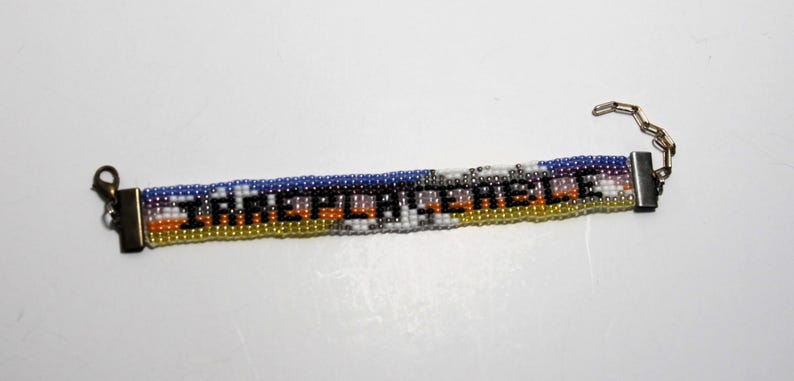 Pu&ograve; includere: Un braccialetto di perline multicolori con una chiusura argentata e una catena. Le perline compongono la parola "remarkable" in nero.