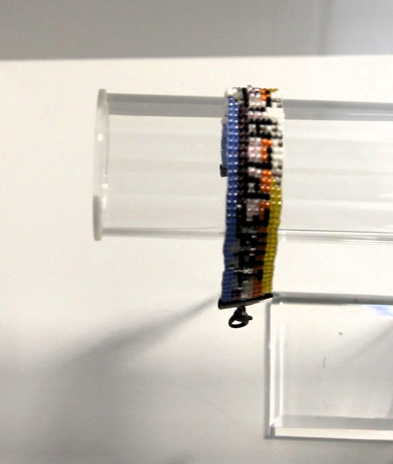 Pu&ograve; includere: Un braccialetto di perline multicolori con una chiusura argentata. Il braccialetto presenta un motivo di perline blu, bianche, arancioni e gialle.