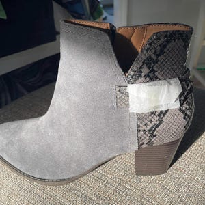 May include: A white ceramic mug with a black handle and the text "But First, Coffee" in a bold, black font. The mug is filled with a dark liquid, likely coffee, and sits on a light-colored surface.