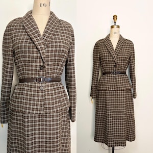 May include: A vintage brown and beige checked skirt suit, comprising a blazer and a knee-length skirt. The blazer features a notched collar, long sleeves, and a single-button fastening. A brown belt defines the waist. The suit is displayed on a mannequin.