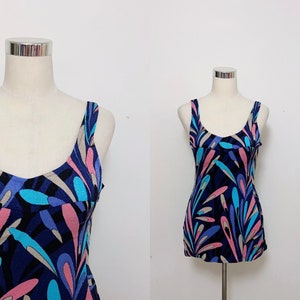 May include: A sleeveless, blue, pink and white patterned swimsuit with a scoop neck. The swimsuit is on a white mannequin.