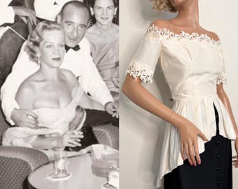 May include: Vintage off-the-shoulder top with lace trim on the sleeves and neckline, paired with a black skirt. The top has a peplum design and a button-down front. The image also includes a black and white photo of a couple.
