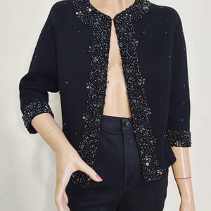 May include: A black cardigan with a beaded trim around the neckline, cuffs, and front edges. The beads are black and silver.