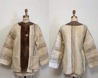 May include: A cream-colored, striped, wool jacket with a brown suede panel down the front. The jacket has a stand-up collar, long sleeves, and two patch pockets. It has three brown buttons down the front.