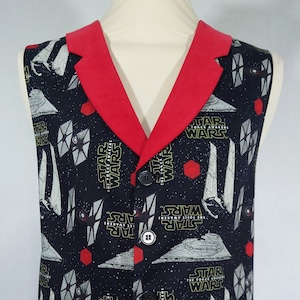 Puede incluir: Un chaleco negro con cuello rojo y un patrón repetido de naves espaciales de Star Wars: El Despertar de la Fuerza y el logotipo de Star Wars.