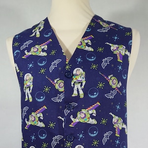 Op de afbeelding: Een donkerblauw vest met een herhalend patroon van Buzz Lightyear uit Toy Story. Het patroon bevat ook sterren, planeten en ruimteschepen.