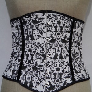 May include: A black and white corset with a Halloween-themed print featuring witches, cats, and cauldrons. The corset has a black satin trim and silver metal eyelets.