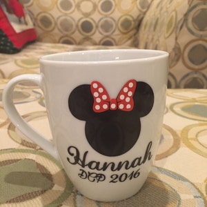 May include: White ceramic mug with a black and red Minnie Mouse design. The mug has the name "Hannah" and the text "DCP 2016" printed on it.