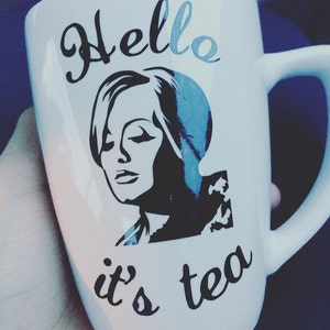 May include: White ceramic mug with a black and white image of a woman and the text "Hello it's tea".