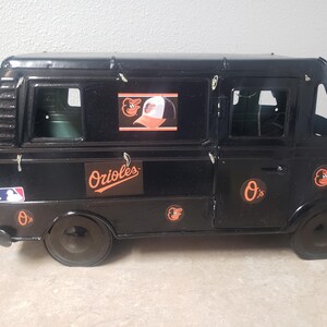 May include: Black toy van featuring the Baltimore Orioles logo and colors. The van has multiple windows and the Orioles logo on the side. The MLB logo is also visible. A collectible item for baseball fans.