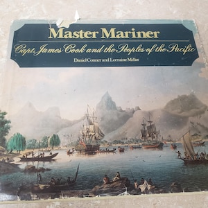 May include: A vintage book cover titled "Master Mariner" with the subtitle "Capt. James Cook and the Peoples of the Pacific." The cover features a detailed illustration of ships sailing on a body of water, with mountains in the background.