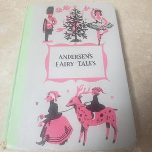 May include: Vintage book titled "Andersen's Fairy Tales" with a light green spine. The cover features illustrations of a soldier, a ballerina, and figures riding a pink spotted deer. The title is in a pink frame on a white background.