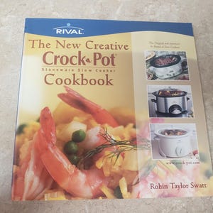 May include: The New Creative Crock-Pot Cookbook by Robin Taylor Swatt. The cover features a vibrant image of shrimp and rice. The cookbook is for stoneware slow cookers. The Rival logo is at the top.