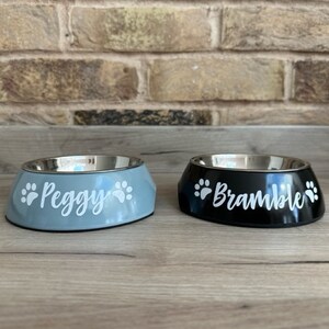 May include: Two personalized pet bowls, one blue and one black, with paw prints and names "Peggy" and "Bramble" printed on them.