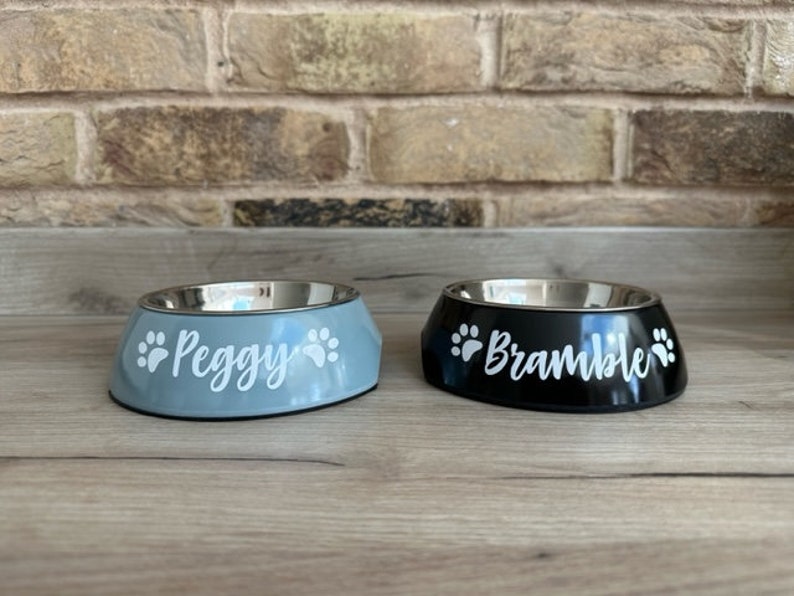 May include: Two personalized pet bowls, one blue and one black, with paw prints and names "Peggy" and "Bramble" printed on them.