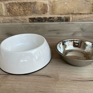 May include: Two pet bowls, one white ceramic and one silver metal.