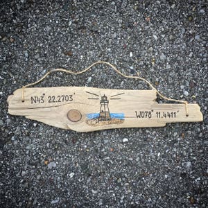 May include: A wooden sign with a lighthouse drawing and coordinates N43&deg; 22.2703' W078&deg; 11.4411' written on it.