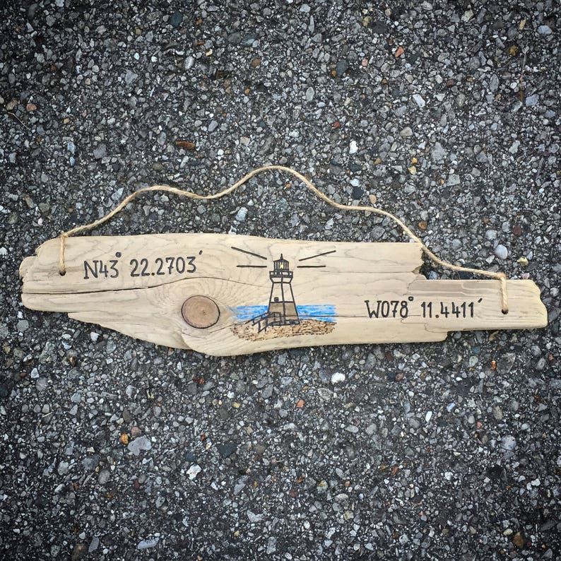 May include: A wooden sign with a lighthouse drawing and coordinates N43&deg; 22.2703' W078&deg; 11.4411' written on it.