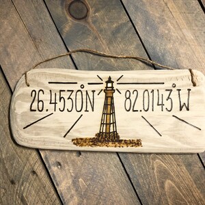May include: A wooden sign with a lighthouse design and the coordinates 26.4530N 82.0143W burned into the surface.