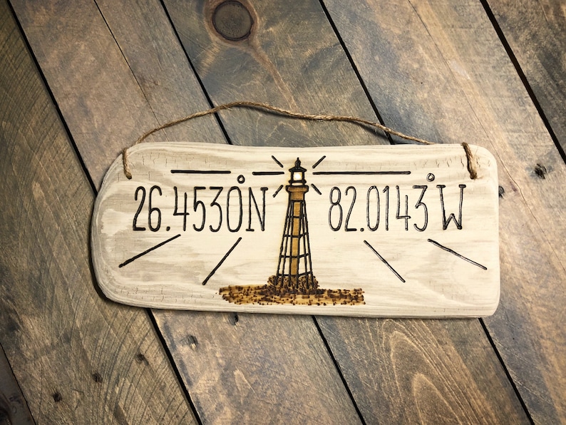 May include: A wooden sign with a lighthouse design and the coordinates 26.4530N 82.0143W burned into the surface.
