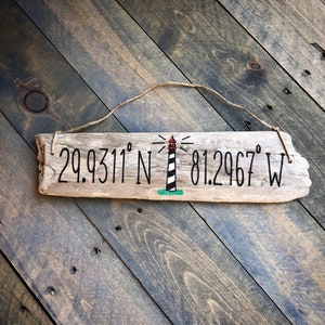 May include: A weathered piece of driftwood with a painted lighthouse and the coordinates 29.9311&deg; N 81.2967&deg; W.