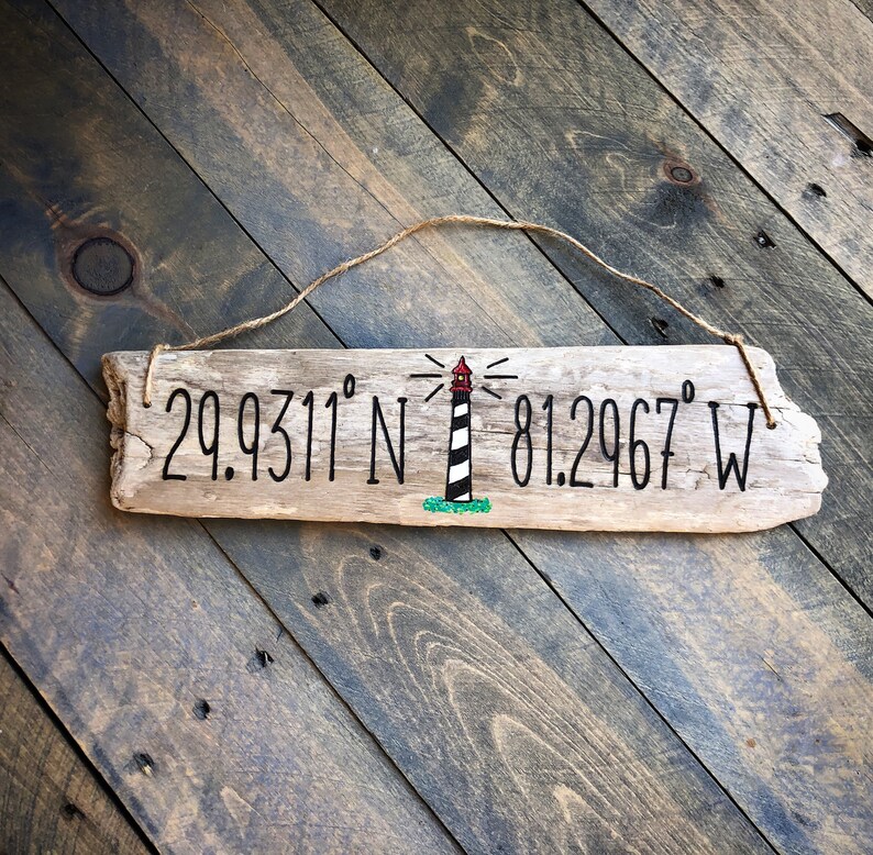 May include: A weathered piece of driftwood with a painted lighthouse and the coordinates 29.9311&deg; N 81.2967&deg; W.