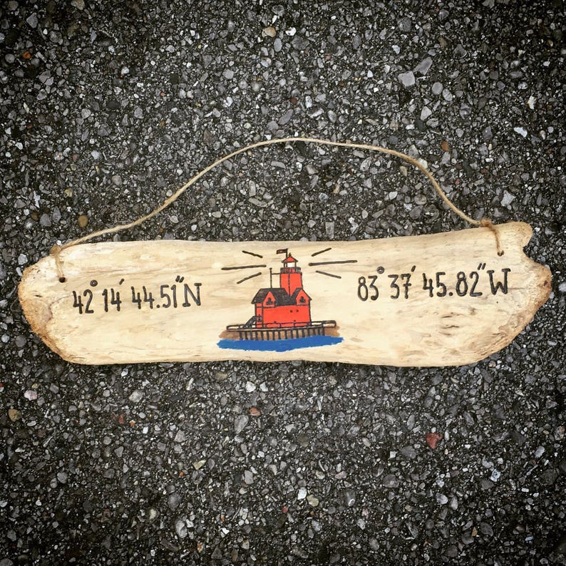 May include: A wooden sign with a painted lighthouse and coordinates: 42&deg; 14' 44.51" N 83&deg; 37' 45.82" W.