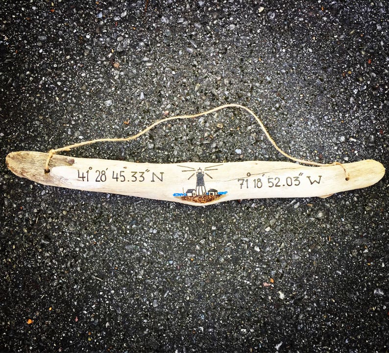 May include: A piece of driftwood with a lighthouse drawing and the coordinates "41&deg; 28' 45.33" N 71&deg; 18' 52.03" W" written on it.