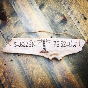 May include: A piece of driftwood with the coordinates 34.6226&deg;N 76.5245&deg;W and a lighthouse illustration burned into the wood.